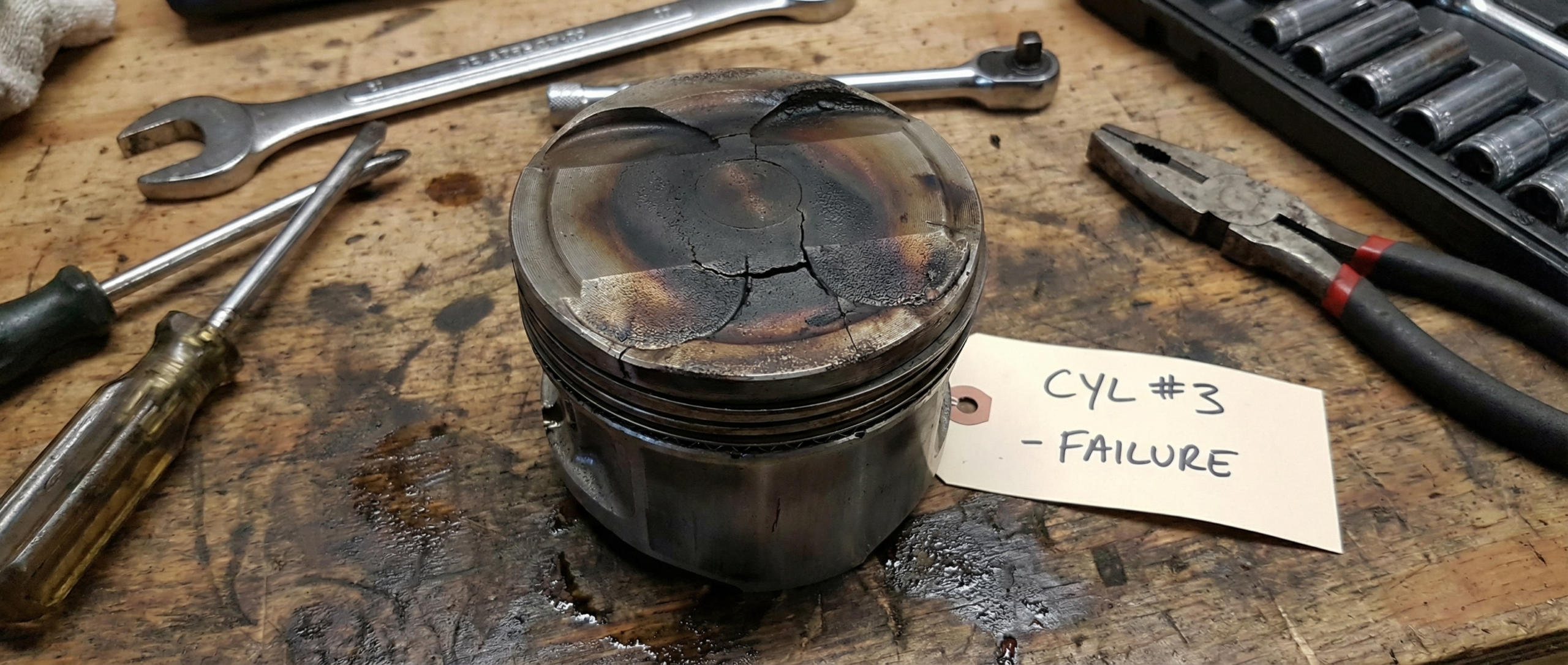 A worn, cracked, or scorched piston placed on a mechanic’s table with tools around it. Perfect for highlighting “problems
